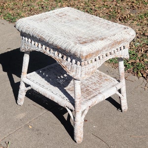 May include: White wicker end table with a lower shelf. The table has a decorative beaded trim around the top edge.