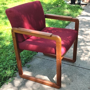 May include: A burgundy upholstered chair with a wooden frame. The chair has a square back and arms, and the frame is made of dark wood.