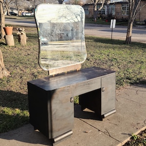 May include: A dark wood vanity with a large, oval-shaped mirror. The vanity has two drawers and two doors. The mirror is attached to the vanity with a metal frame.
