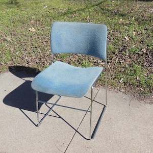 May include: A blue upholstered chair with a chrome frame. The chair has a simple design with a slightly curved back and a square seat.