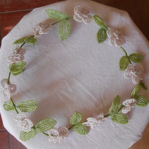 May include: A delicate beaded garland with white flowers and green leaves. The garland is made of small beads and is perfect for adding a touch of elegance to any occasion.