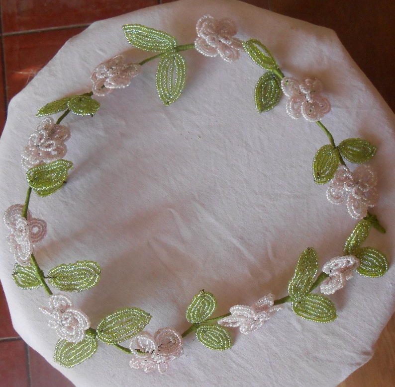 May include: A delicate beaded garland with white flowers and green leaves. The garland is made of small beads and is perfect for adding a touch of elegance to any occasion.