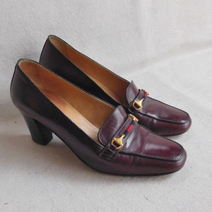 May include: A pair of burgundy leather heeled shoes with gold buckles and red and blue trim. The shoes have a pointed toe and a block heel.