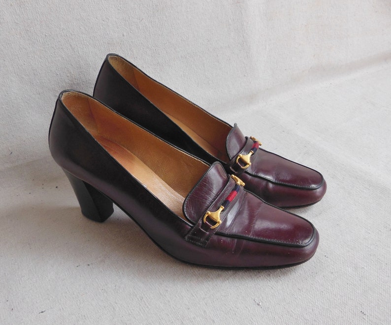 May include: A pair of burgundy leather heeled shoes with gold buckles and red and blue trim. The shoes have a pointed toe and a block heel.