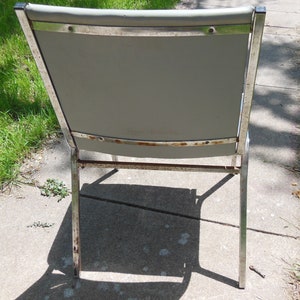 May include: A vintage metal chair with a gray fabric seat and chrome legs. The chair has a simple design and is in good condition.