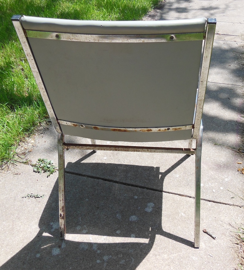 May include: A vintage metal chair with a gray fabric seat and chrome legs. The chair has a simple design and is in good condition.