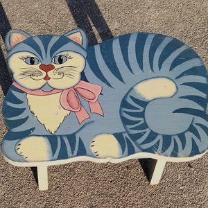 May include: A blue and white painted wooden cat stool with pink ribbon and white legs.