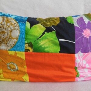 May include: Rectangular patchwork pillow featuring a variety of colorful floral and geometric patterns. The pillow's design includes squares of blue, orange, black, and pink fabrics, creating a vibrant and eclectic aesthetic. The pillow is filled and ready to use.