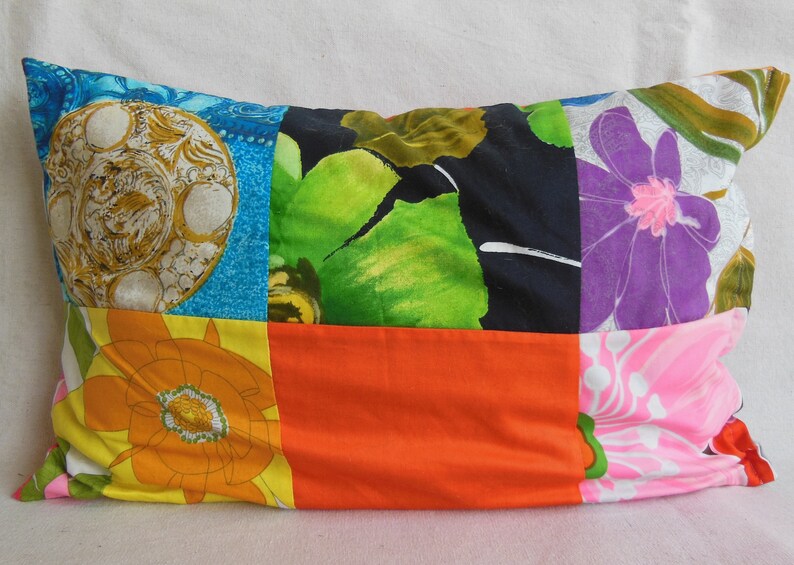 May include: Rectangular patchwork pillow featuring a variety of colorful floral and geometric patterns. The pillow's design includes squares of blue, orange, black, and pink fabrics, creating a vibrant and eclectic aesthetic. The pillow is filled and ready to use.