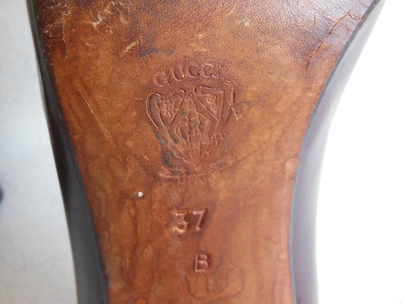 May include: Close-up of the sole of a brown leather shoe with the Gucci logo and the size 37 stamped on the bottom.