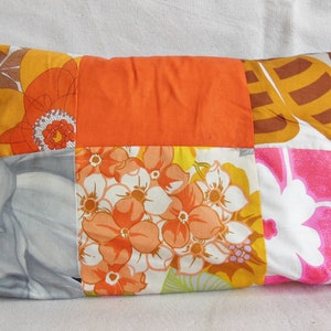 May include: Rectangular patchwork pillow featuring a vibrant mix of floral patterns in orange, yellow, pink, and gray. The pillow's design includes large flower motifs and solid orange squares, creating a retro, bohemian aesthetic. A decorative accent for a bed or sofa.