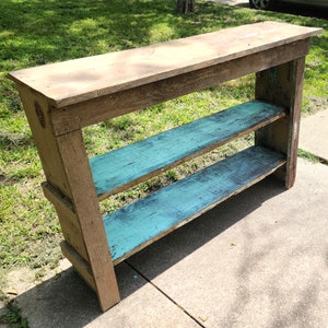 May include: A rustic wooden console table with two shelves painted teal blue. The table has a natural wood finish and is perfect for displaying decorative items or storing books.