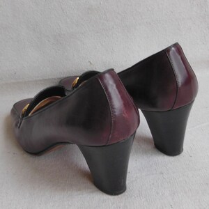 May include: A pair of burgundy leather heeled shoes with a gold buckle detail. The shoes have a black heel and a pointed toe.