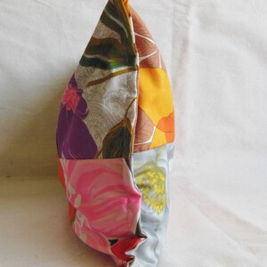 May include: A patchwork pillow with a variety of floral patterns in shades of pink, purple, orange, and gray. The pillow is rectangular and appears to be made of fabric scraps sewn together. The pillow is on a white surface.