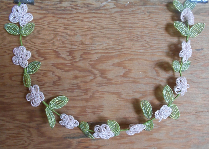 May include: A beaded garland with white flowers and green leaves. The garland is made of small beads and is strung together to form a continuous loop.