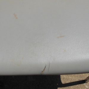 May include: A close-up of a gray chair seat with a small tear and some light brown stains.
