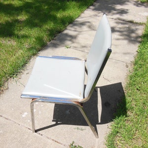 May include: A gray metal chair with a chrome frame. The chair is sitting on a concrete sidewalk.
