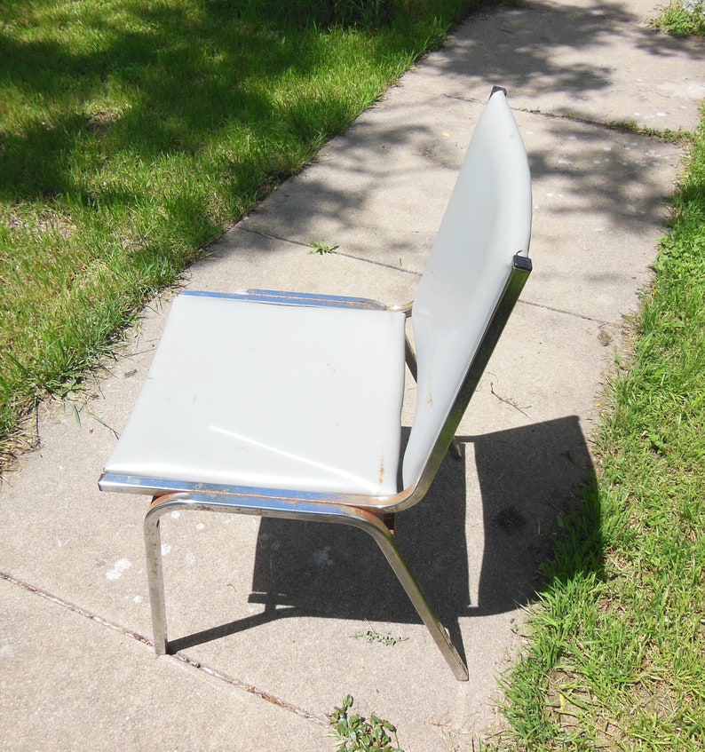 May include: A gray metal chair with a chrome frame. The chair is sitting on a concrete sidewalk.