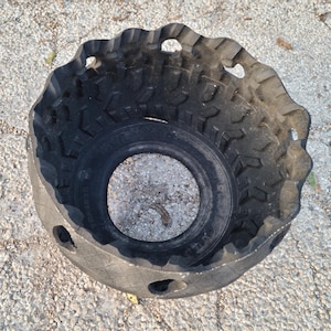 May include: A black tire cut in half and turned into a planter. The tire has a rough tread pattern and several holes cut into the side.