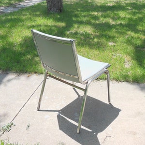 May include: A silver metal chair with a light gray fabric seat. The chair is sitting on a concrete patio.