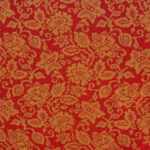 May include: Close-up of a red fabric with a repeating pattern of gold floral designs. The flowers and leaves are intricately detailed, creating a textured appearance. The background is a solid, vibrant red.