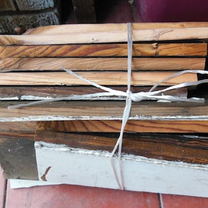 May include: A stack of wooden boards tied together with white string. The boards are various shades of brown and have a natural wood grain.