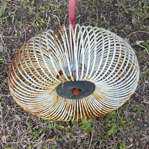 May include: A white metal spring toy with rust showing on the surface. The spring is coiled into a circle shape.