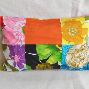 May include: Rectangular patchwork pillow featuring a vibrant mix of floral patterns and solid colors. The design includes pink, orange, yellow, green, and blue fabrics, creating a colorful and eclectic aesthetic. The pillow is a decorative home accent.