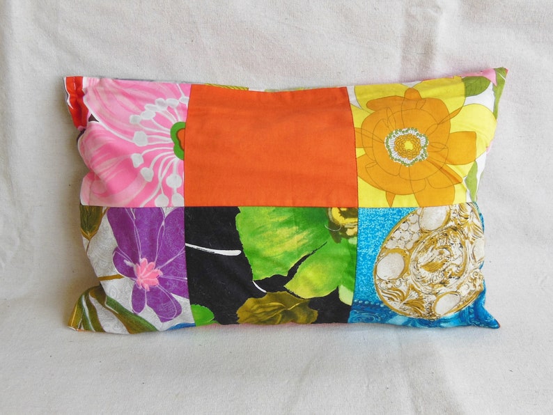 May include: Rectangular patchwork pillow featuring a vibrant mix of floral patterns and solid colors. The design includes pink, orange, yellow, green, and blue fabrics, creating a colorful and eclectic aesthetic. The pillow is a decorative home accent.