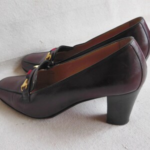 May include: A pair of burgundy leather heeled shoes with gold accents and a red and blue trim. The shoes have a block heel.