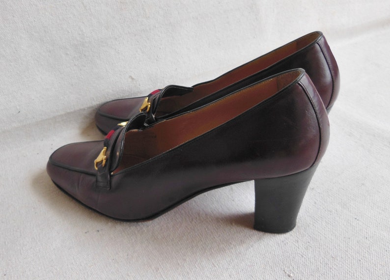 May include: A pair of burgundy leather heeled shoes with gold accents and a red and blue trim. The shoes have a block heel.