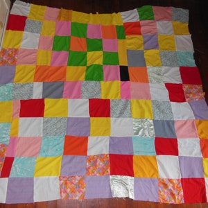 May include: A patchwork quilt made of various colored squares, including red, yellow, orange, green, blue, purple, and white.