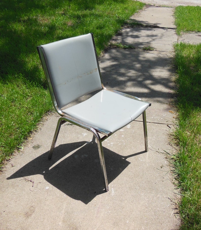 May include: A silver metal chair with a light gray padded seat. The chair is on a concrete surface.
