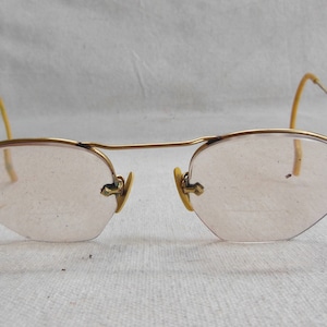 May include: A pair of gold-rimmed glasses with pink tinted lenses. The glasses have a simple, classic design.