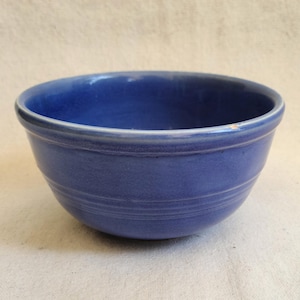 May include: A blue ceramic bowl with a rounded shape. The bowl has a smooth, glossy finish and a slightly textured surface. Two horizontal lines encircle the bowl's exterior. The bowl is a solid, vibrant blue color.