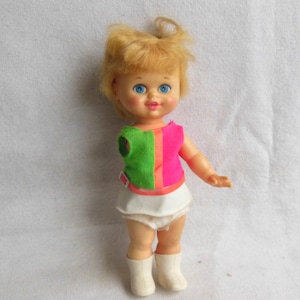 May include: A vintage doll with blonde hair, blue eyes, and a pink and green outfit. The doll is wearing white boots and a white skirt.