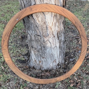 May include: A circular wooden frame with a natural light brown wood grain finish. The frame features a smooth, rounded profile and is constructed from multiple segments joined together, displaying visible wood patterns throughout the entire ring.