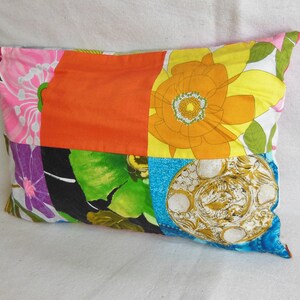 May include: A rectangular patchwork pillow featuring a vibrant mix of floral and geometric patterns. The pillow showcases squares of orange, pink, yellow, blue, and green fabrics, creating a colorful and eclectic design. The pillow is approximately 18 inches long.