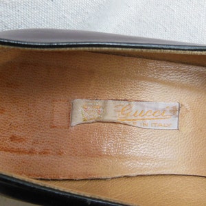 May include: Close-up of the inside of a black leather shoe with a tan leather insole. A white label with the text "Gucci Made in Italy" is visible.
