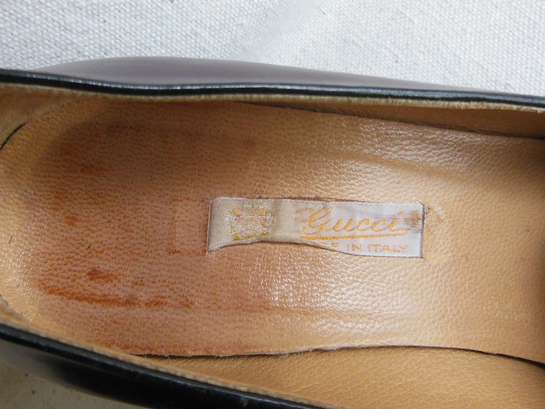 May include: Close-up of the inside of a black leather shoe with a tan leather insole. A white label with the text "Gucci Made in Italy" is visible.