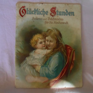 May include: A vintage book cover featuring a mother and child. The mother is wearing a blue dress and a white veil, and she is holding the child in her arms. The child is wearing a white dress and has blonde hair. The book title is "Glückliche Stunden" and the subtitle is "Heiteres und Belehrendes für die Kinderwelt."