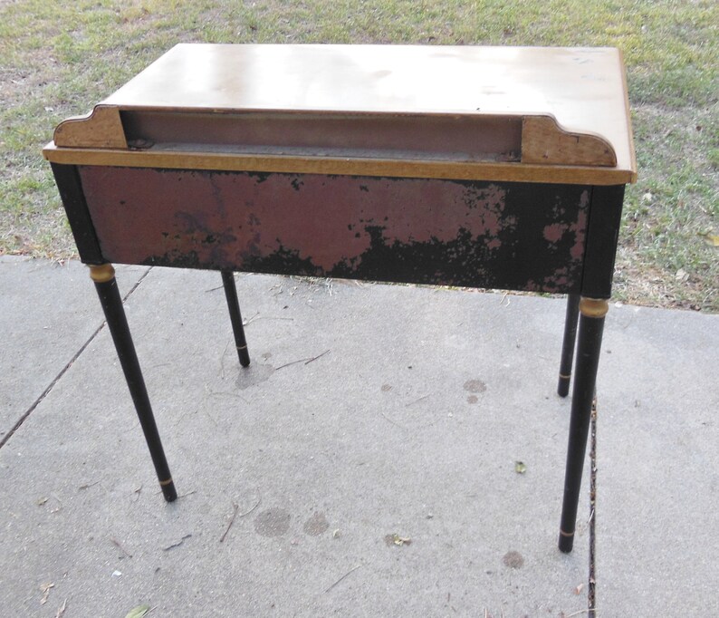 Pu&ograve; includere: Una scrivania in legno vintage con gambe verniciate di nero e dettagli dorati. La scrivania ha una finitura rosso scuro e nera con alcuni segni di usura.