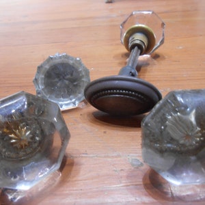 May include: Four antique glass door knobs with a brass and metal base. The knobs are clear glass with a faceted design.