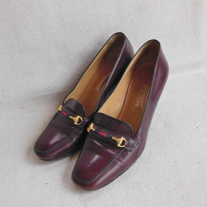 May include: A pair of burgundy leather heeled shoes with gold buckles and a red, white, and blue ribbon detail.