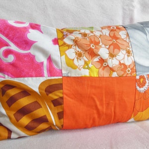 May include: Rectangular decorative pillow with a patchwork design. The pillow features squares of fabric in various floral patterns and solid colors, including pink, orange, white, and brown. The pillow is filled and has a soft appearance.