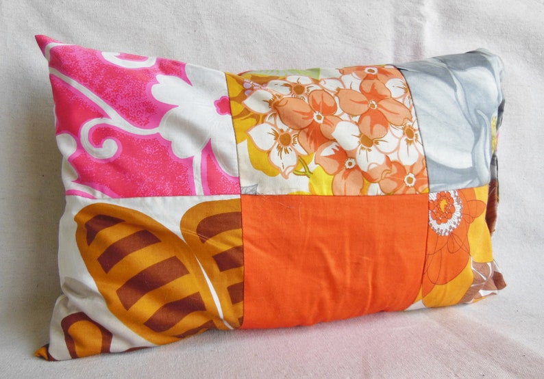 May include: Rectangular decorative pillow with a patchwork design. The pillow features squares of fabric in various floral patterns and solid colors, including pink, orange, white, and brown. The pillow is filled and has a soft appearance.