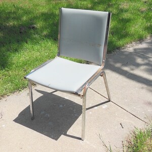 May include: A silver metal chair with a gray fabric seat. The chair has a simple design with a straight back and four legs.