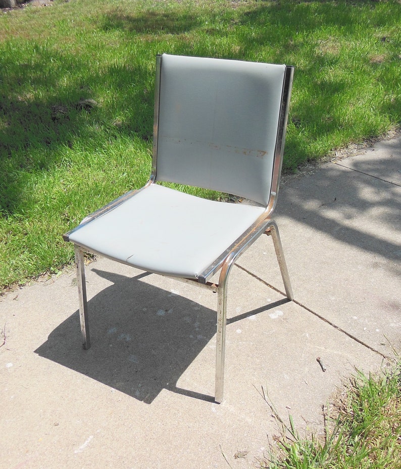 May include: A silver metal chair with a gray fabric seat. The chair has a simple design with a straight back and four legs.