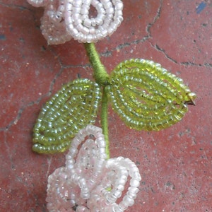May include: A beaded flower garland with white flowers and green leaves. The garland is made of small, round beads and is strung together on a green thread.
