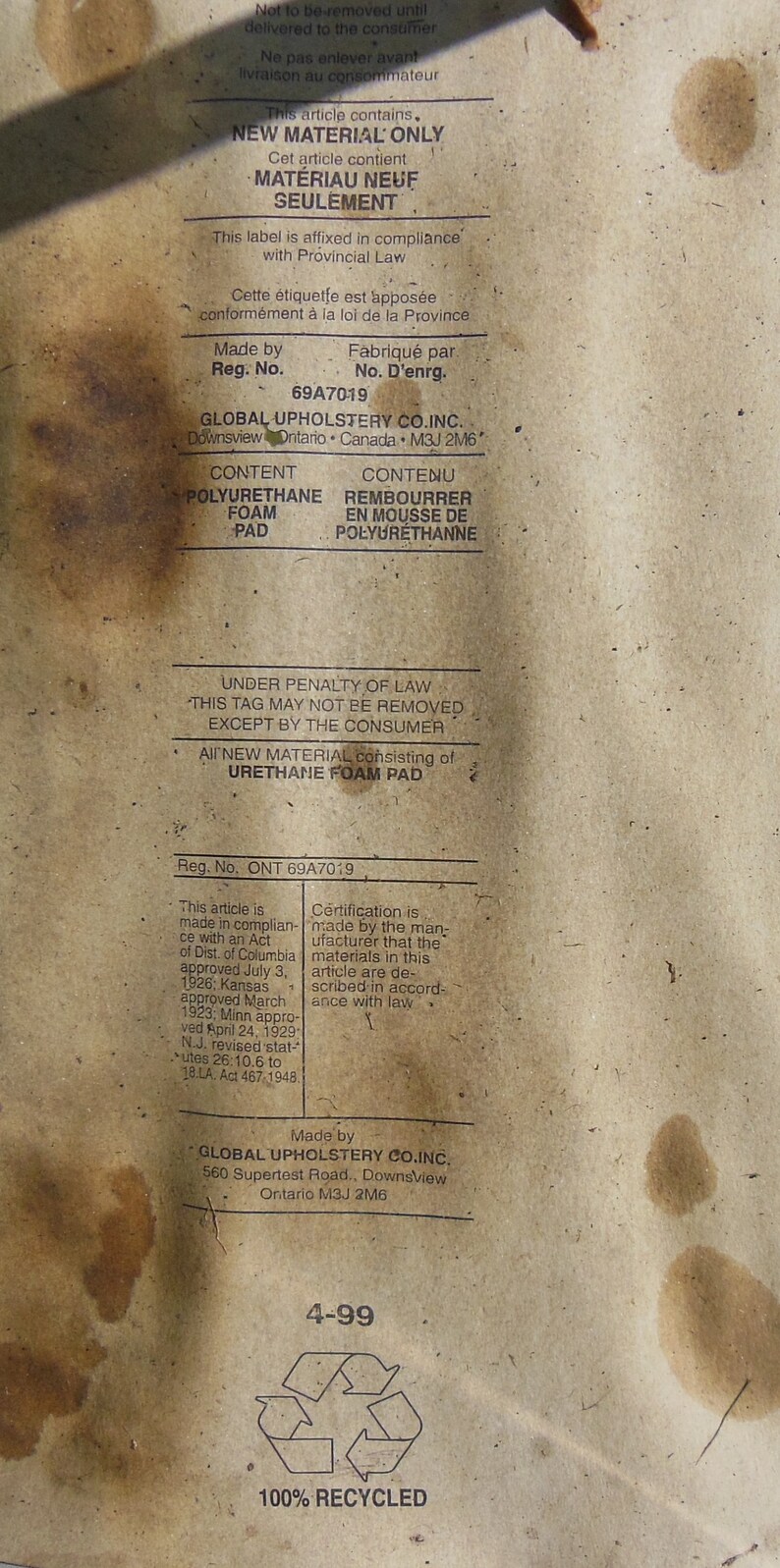 May include: A brown paper tag with white text, indicating that the product contains new material. The tag is labeled "New Material Only" and includes the company name "Global Upholstery Co. Inc." and the address "560 Supertest Road, Downsview Ontario M3J 2M6". The tag also includes the text "Under Penalty of Law This Tag May Not Be Removed Except By The Consumer" and "All New Material Consisting of Urethane Foam Pad".